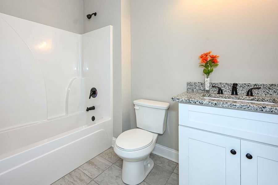 White bathroom with tub, toilet, vanity, and orange flowers.