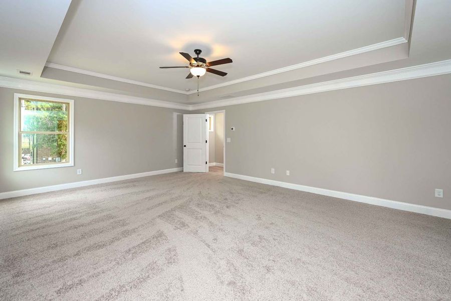 Empty bedroom with beige carpet, light grey walls, and a ceiling fan.
