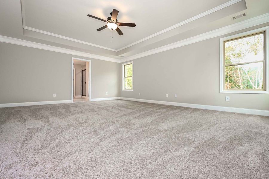 Empty bedroom with gray carpet, walls, and white trim. Features a ceiling fan and two windows.