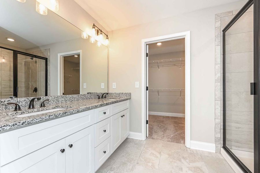 Modern bathroom with white cabinets, granite countertop, and glass shower.