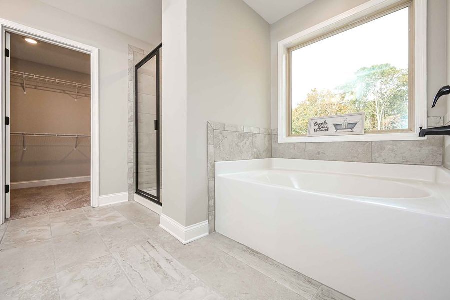 Bathroom with a white tub, shower, and walk-in closet. Light gray walls and window.