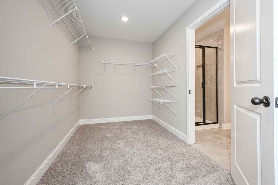 Empty walk-in closet with wire shelves and carpet, with a door to a bathroom.