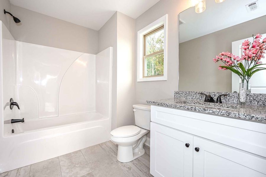 A bathroom with white fixtures, gray walls, and a countertop with pink flowers.