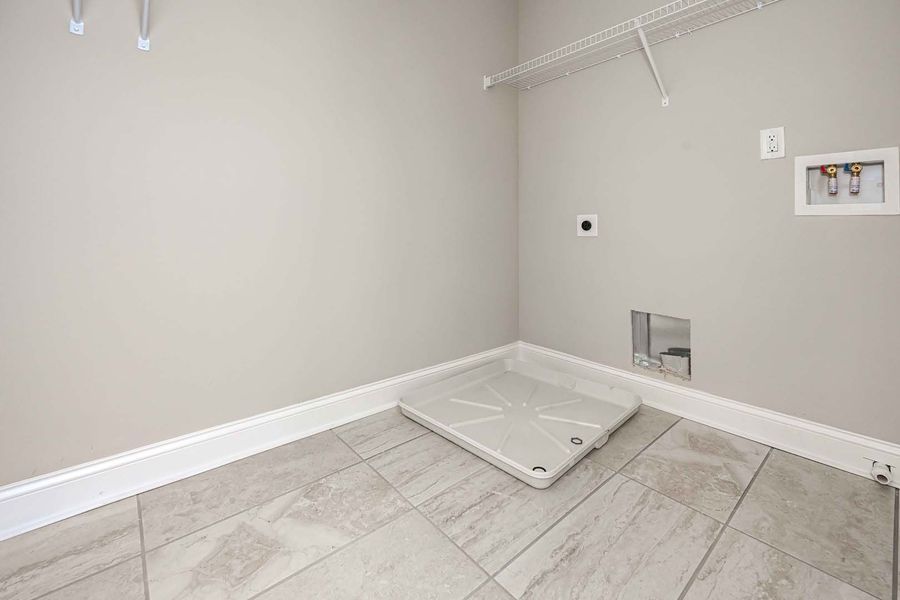 Laundry room with gray walls, tiled floor, and a utility tray. White trim, electrical outlet, and wire shelf.