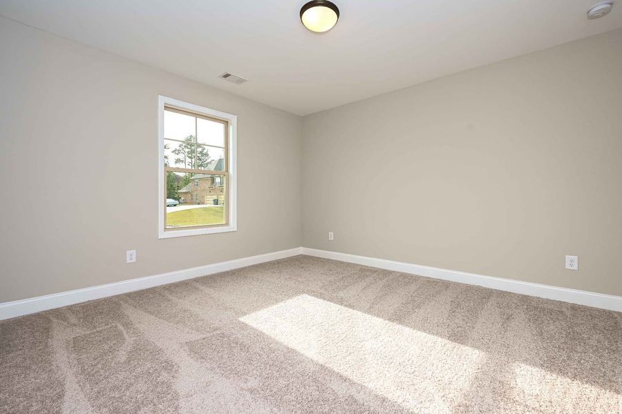 Empty bedroom with beige carpet, tan walls, and a window letting in sunlight.