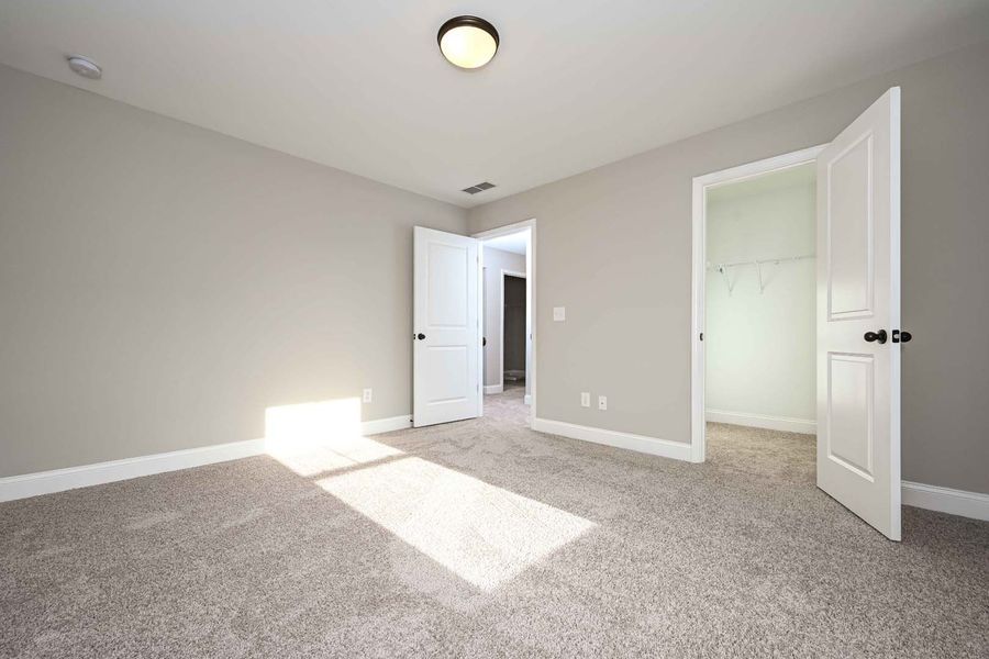 Empty bedroom with gray walls, carpet, and three white doors.