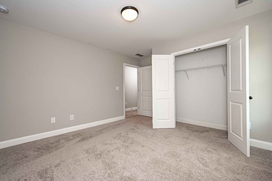 Empty bedroom with gray walls, carpet, and closet with open white doors.