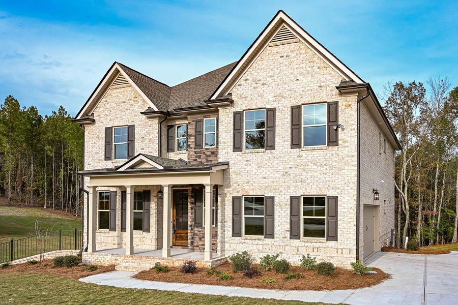 Two-story brick house with dark shutters and a porch on a bright, sunny day.