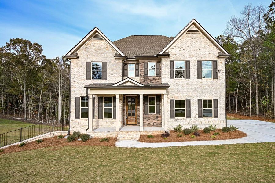 Two-story brick house with brown shutters and door, on a lawn with trees in the background.