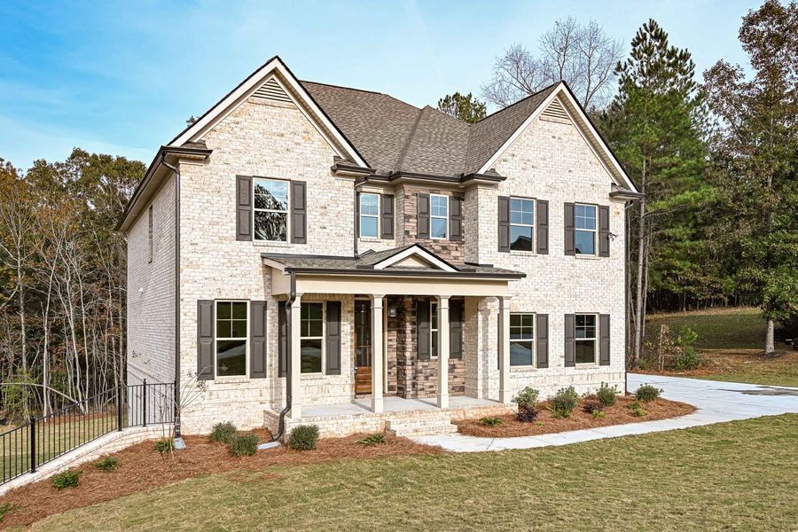 Two-story brick house with brown roof, shutters, and front porch; situated on a grassy hill with driveway.