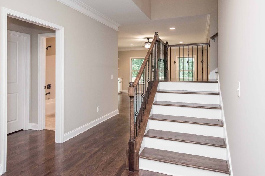 Hallway with dark wood floor, staircase with metal railing, and a door on the left.