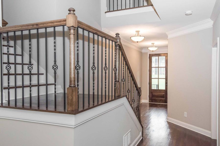 Staircase with black iron railing, wood trim, and dark wooden floors, leading to a doorway.