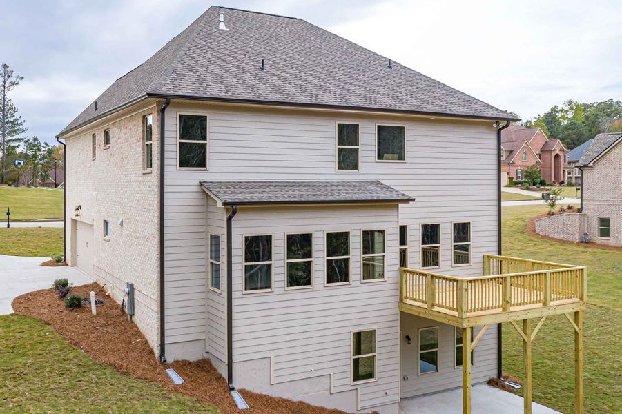 Back of a two-story house with a deck, light siding, and brick. Overcast day in a residential area.