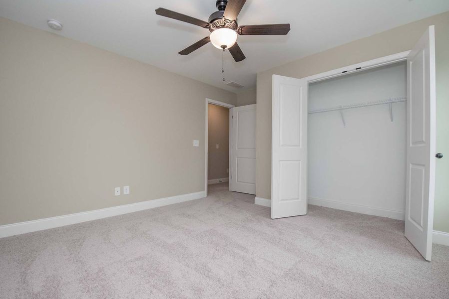 Empty bedroom with beige walls, gray carpet, closet, and ceiling fan.