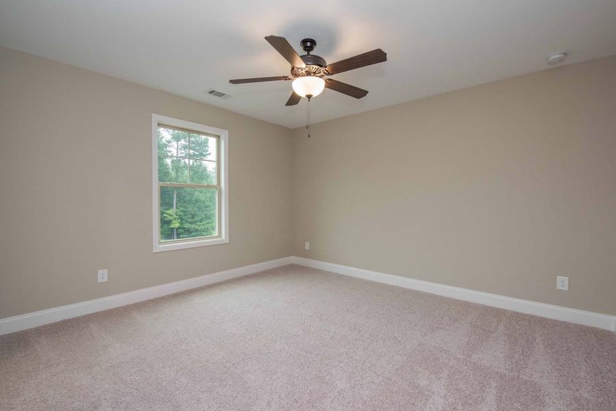 Empty bedroom with tan walls, beige carpet, a window, and ceiling fan.