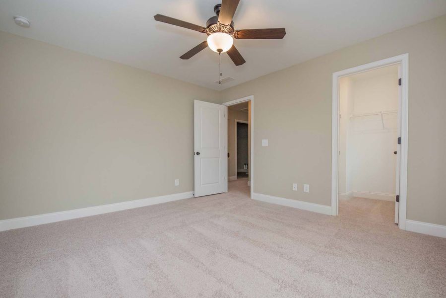 Empty bedroom with beige walls, carpet, and doors. Brown ceiling fan.