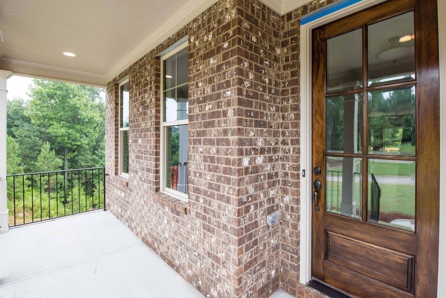 Brick-walled porch with dark wood door and windows, white trim, overlooking a green landscape.