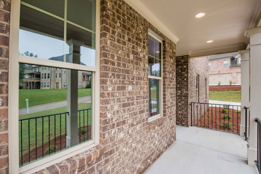 Brick house exterior with a porch and large windows, with a view of a grassy yard and other houses.