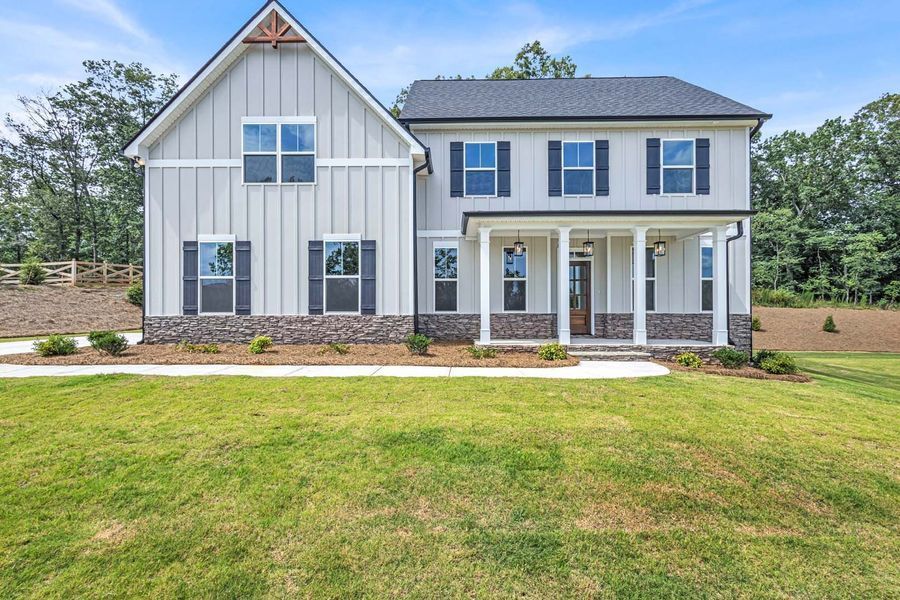 Two-story house with gray siding, brown stone base, dark shutters, white porch columns, and green lawn.