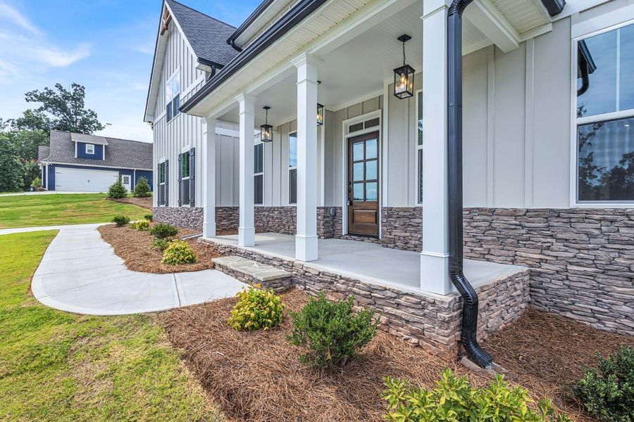 Gray house with covered porch, stone accents, and landscaping along a concrete walkway.