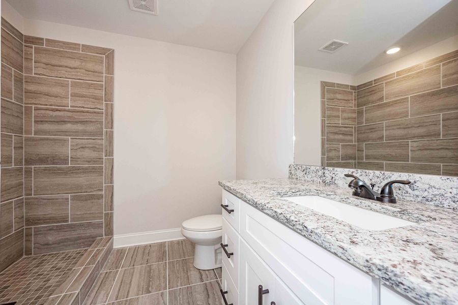 Bathroom with tiled shower and walls, white vanity with granite countertop, and a toilet.