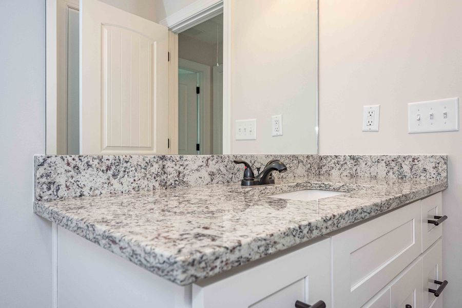 Bathroom vanity with white cabinets, granite countertop, black faucet, and mirror.