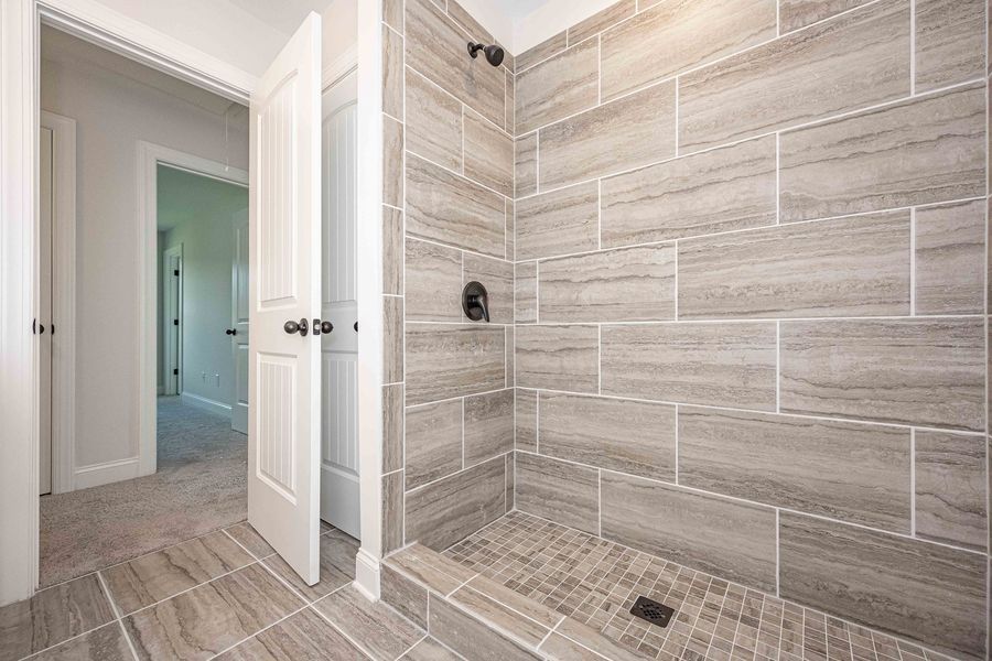 Modern shower with gray tiled walls and floor, black fixtures, open door to hallway.