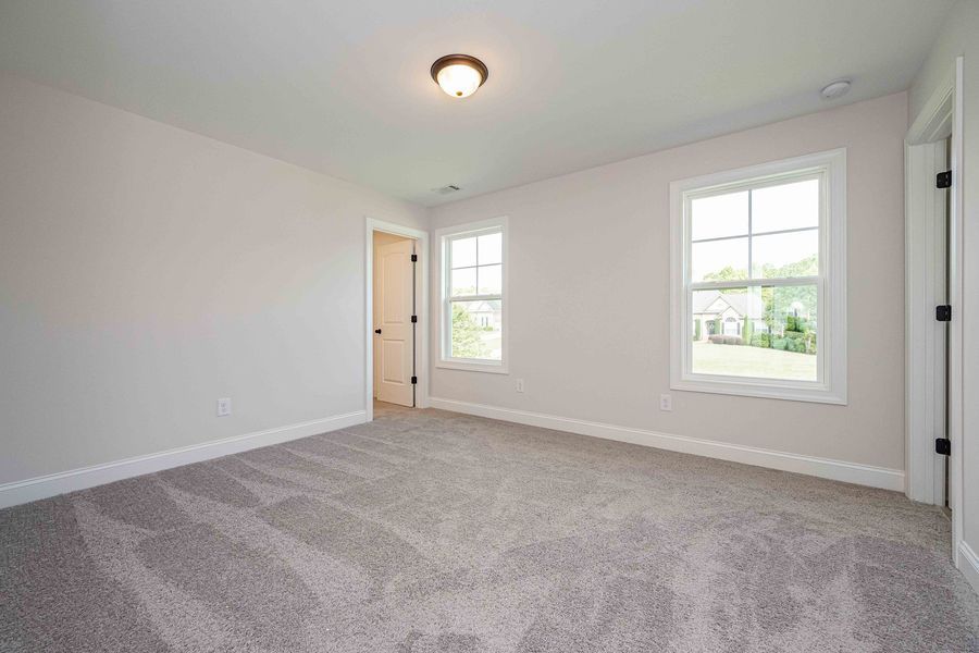 Empty bedroom with gray carpet, two windows, and a doorway.