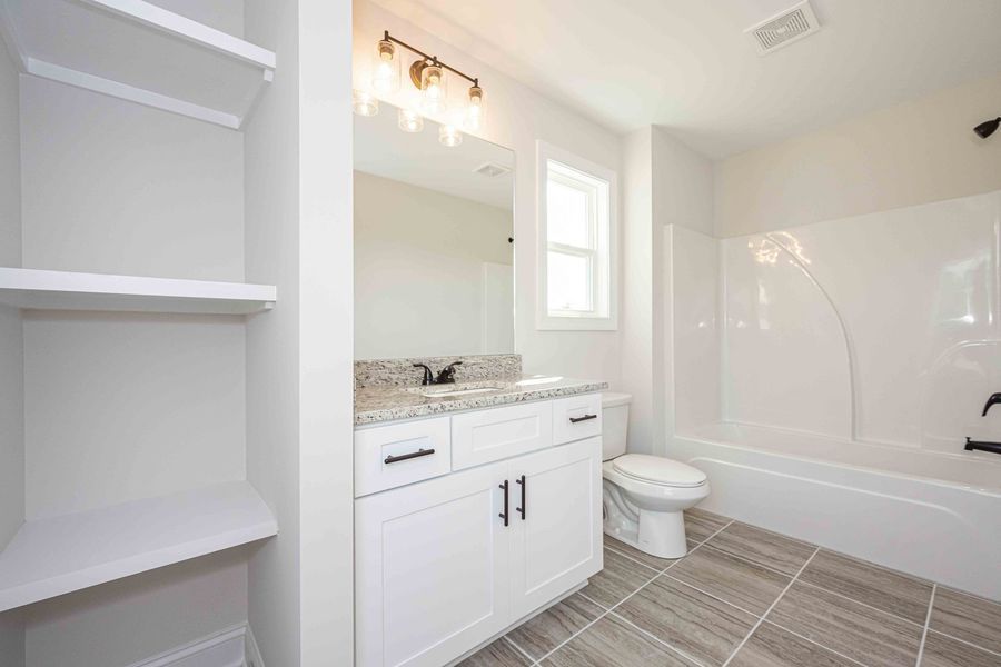 Bathroom with white cabinets, granite countertop, gray tile floor, and white bathtub.
