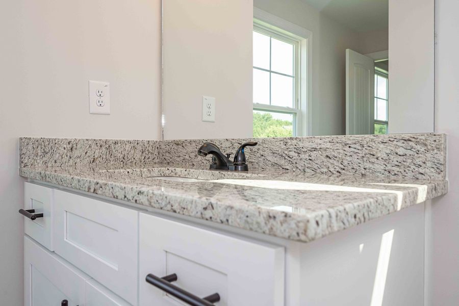White bathroom vanity with granite countertop, black faucet, and mirror.