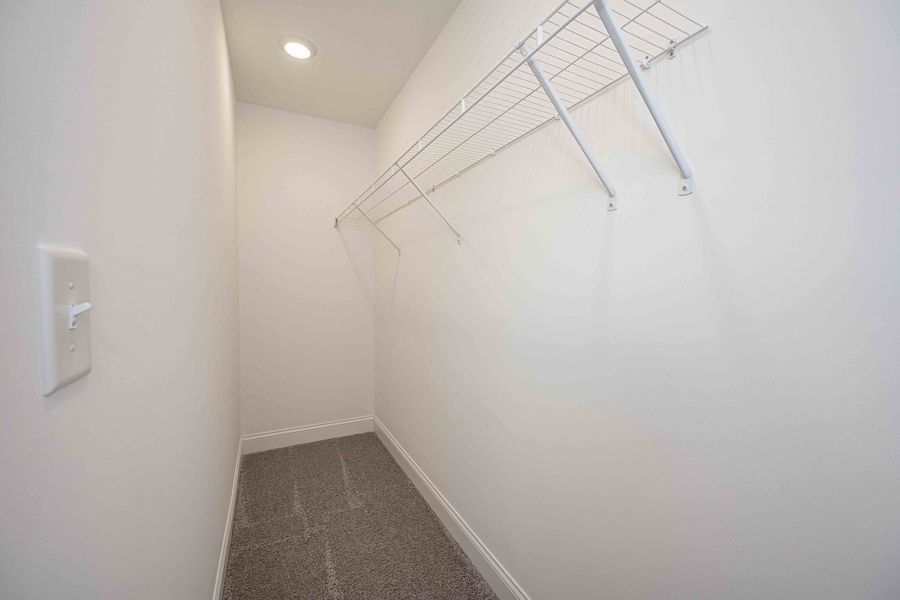 Small, empty white closet with wire shelving and gray carpet. Electrical outlet visible.