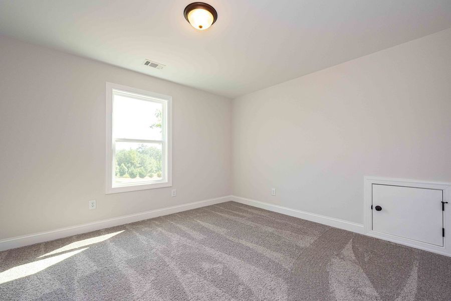 Empty room with gray carpet, white walls, window, and small door.