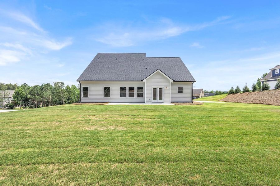 Back of a light-colored house with a dark roof and doors/windows, on a grassy hill under a blue sky.