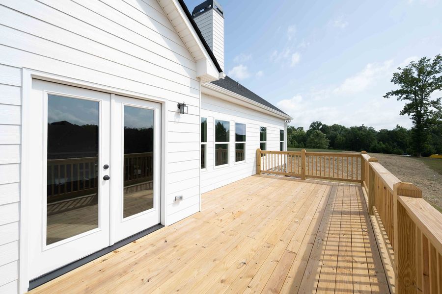 White house with wooden deck, French doors, and a railing overlooking a rural landscape.