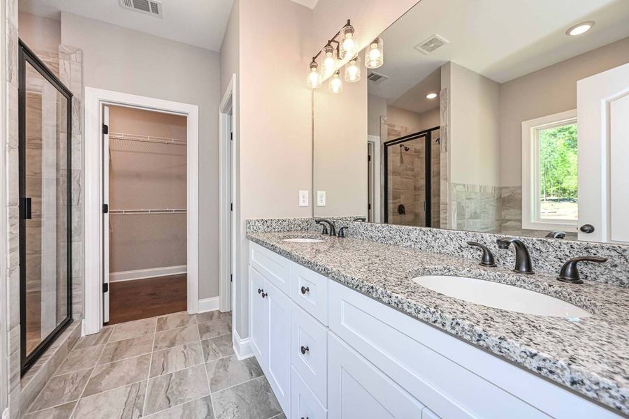 Bathroom with white cabinets, granite countertop, dual sinks, large mirror, and glass shower.