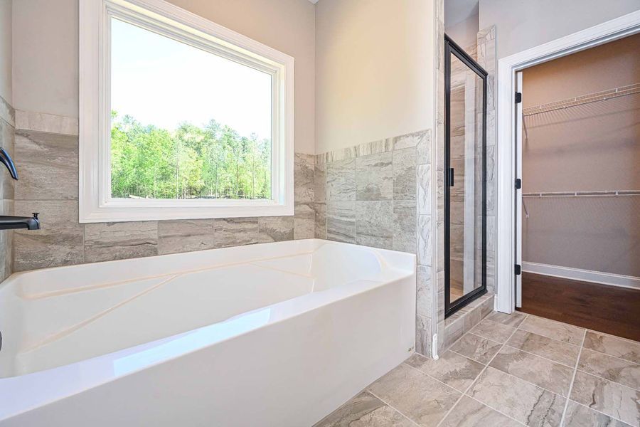 Bathroom with bathtub, window, tiled walls, and walk-in closet.