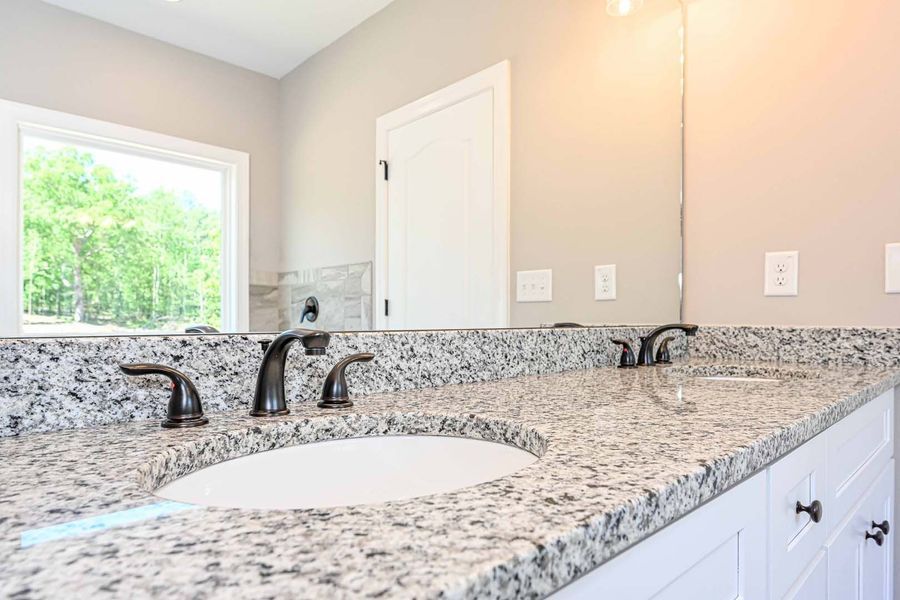Bathroom vanity with granite countertop, dual sinks, dark bronze faucets, and large mirror.