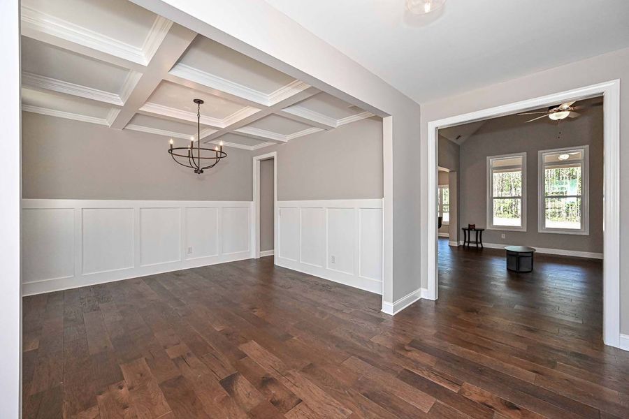 Dining room with wood floors, wainscoting, coffered ceiling, and chandelier.  View into a living space.