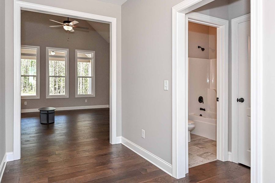 Hallway with open doorway to bedroom, and doorway to bathroom. Hardwood floors. Light grey walls.