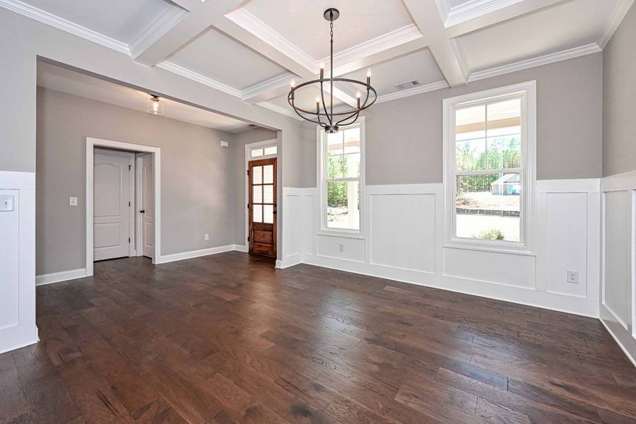 Empty dining room with wood floors, gray walls, white trim, and chandelier.