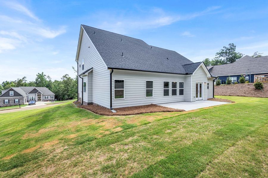 Back view of a white house with a black roof, patio, and grassy yard.