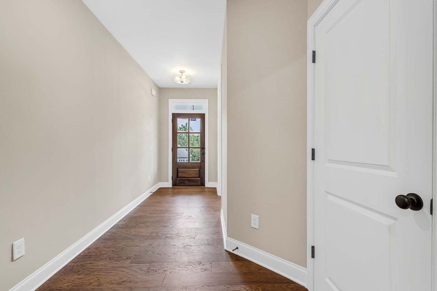 Long hallway with dark wooden door at the end and white door on the right.