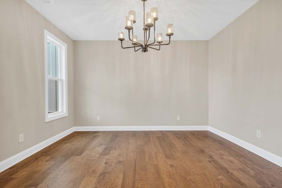 Empty dining room with hardwood floor, neutral walls, window, and chandelier.