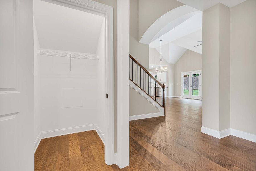 A view of a walk-in closet next to a staircase and living area with hardwood floors.