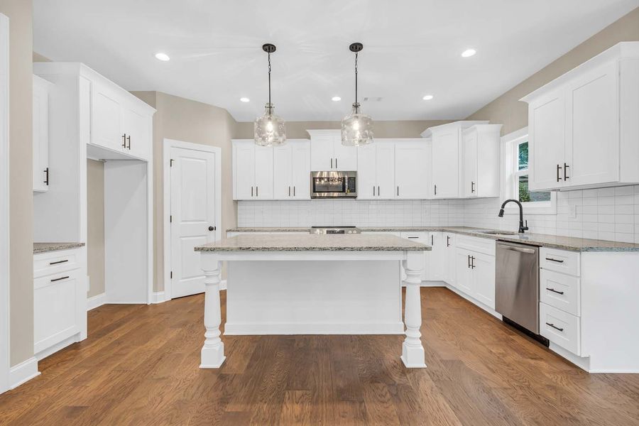 Bright white kitchen with island, wood floor, and stainless steel appliances.