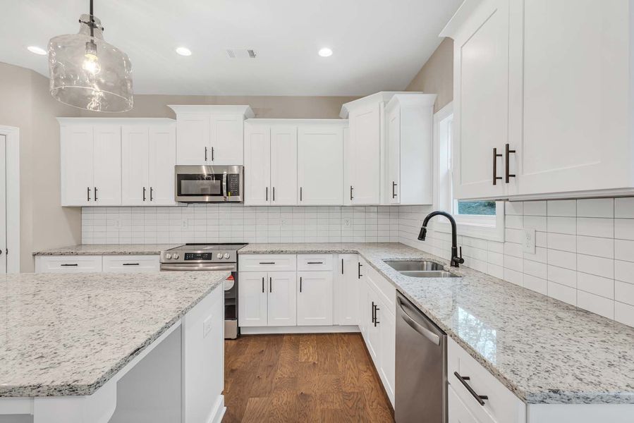 Modern white kitchen with granite countertops, stainless steel appliances, and dark wood floors.