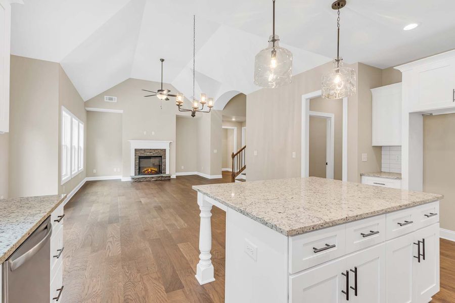 Spacious kitchen with island and vaulted ceiling, leading into a living area with fireplace.