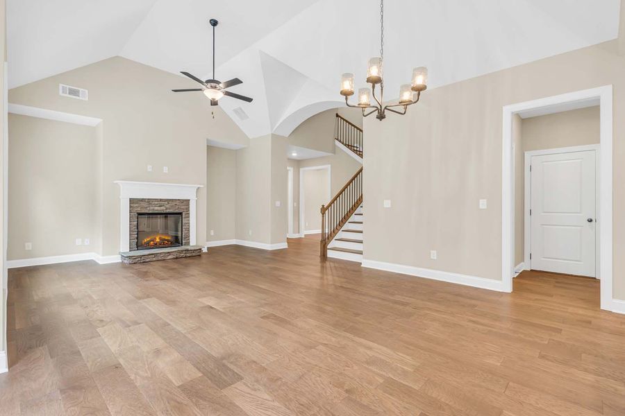 Spacious living room with hardwood floors, fireplace, and chandelier. Vaulted ceiling, neutral walls, and staircase.
