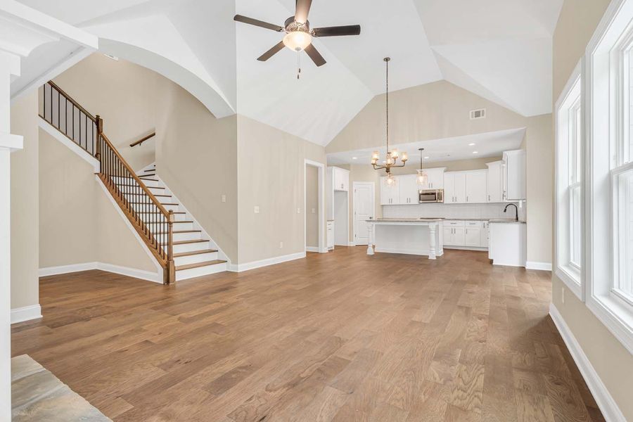 Spacious living room with vaulted ceiling, hardwood floors, staircase, and open kitchen.