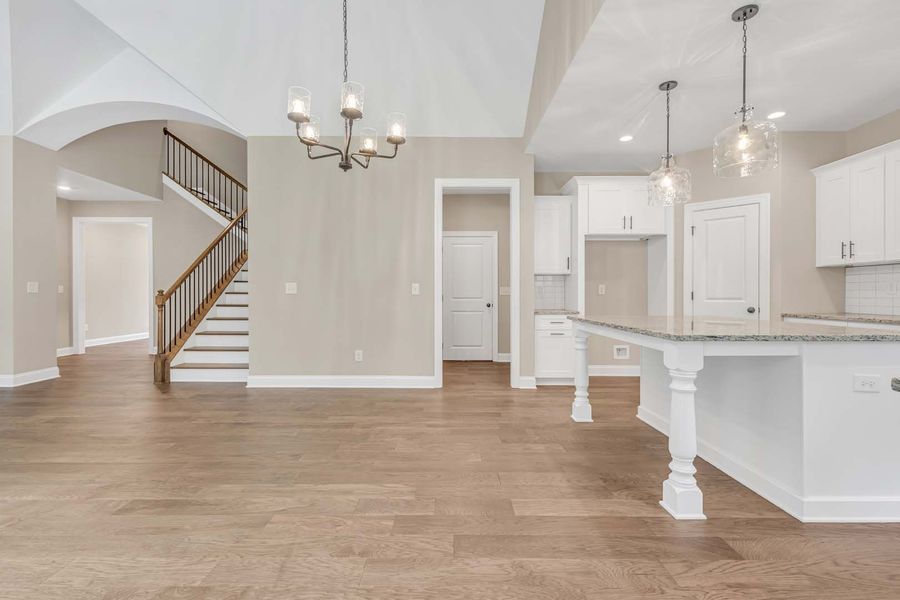 Open-concept kitchen and living area with hardwood floors, white cabinets, and a staircase.